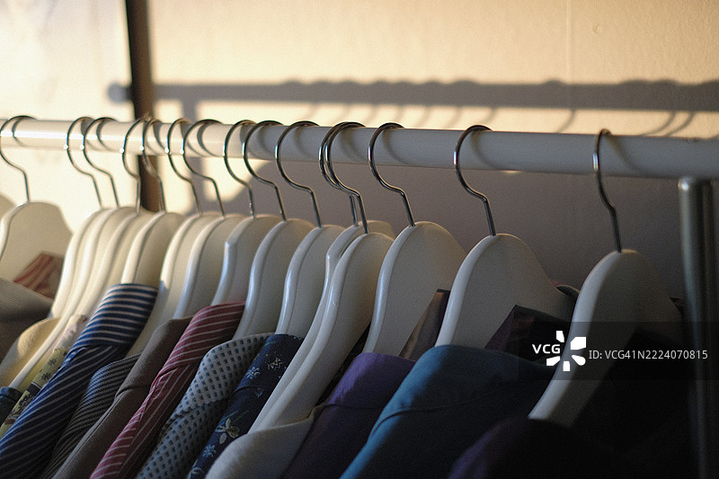 一排挂在衣架上的衣物，沐浴在柔和的阳光中图片素材