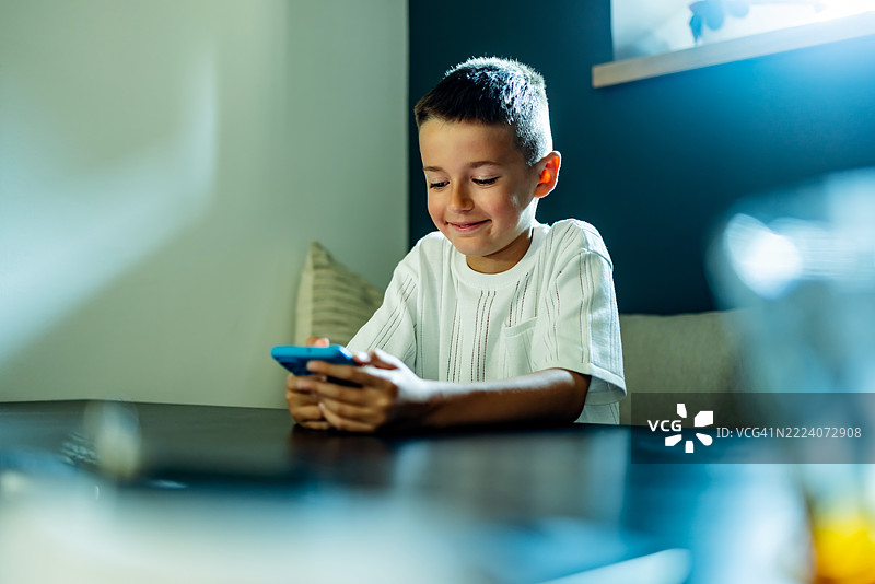 年轻男孩在自然光下微笑着使用智能手机图片素材