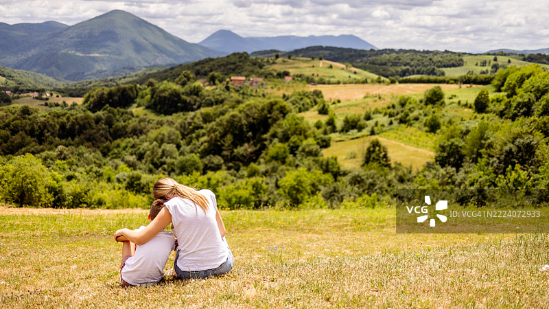 母亲和孩子在宁静的山顶上放松，享受全景山脉美景图片素材