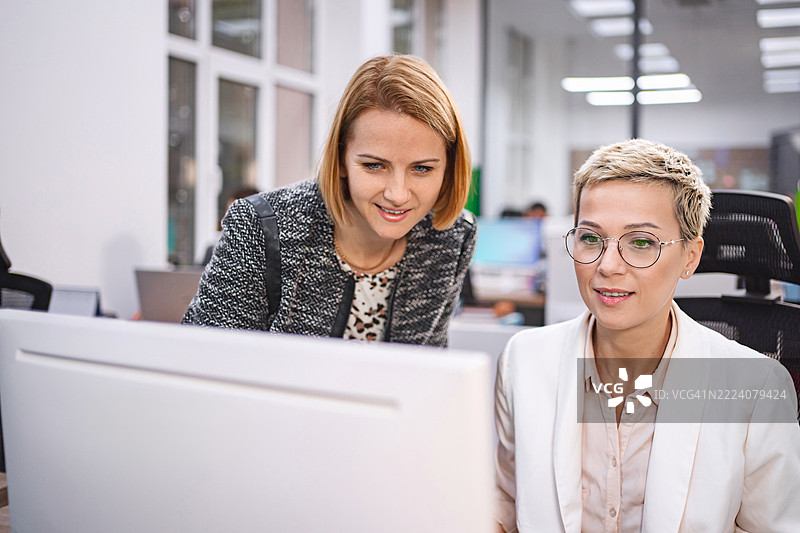 两位女商人在办公室合作，共同查看电脑。图片素材
