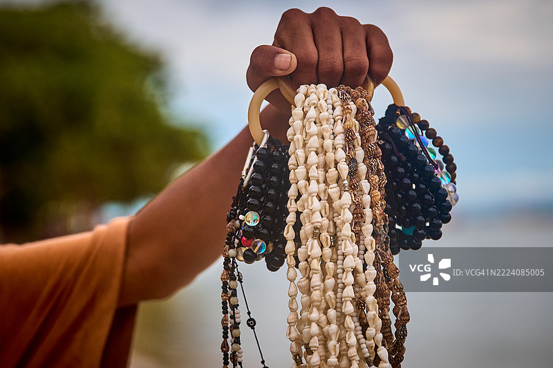 一位纪念品商贩手持一束珠子饰品。图片素材
