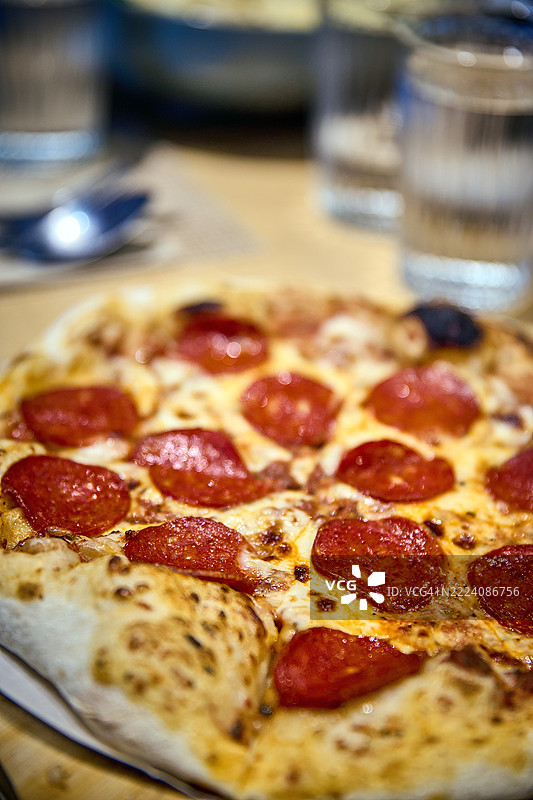 特写镜头捕捉到一整张意大利香肠披萨放在木制餐盘上。图片素材