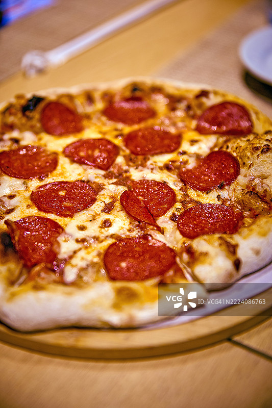 特写镜头捕捉到一整张意大利香肠披萨放在木制餐盘上。图片素材