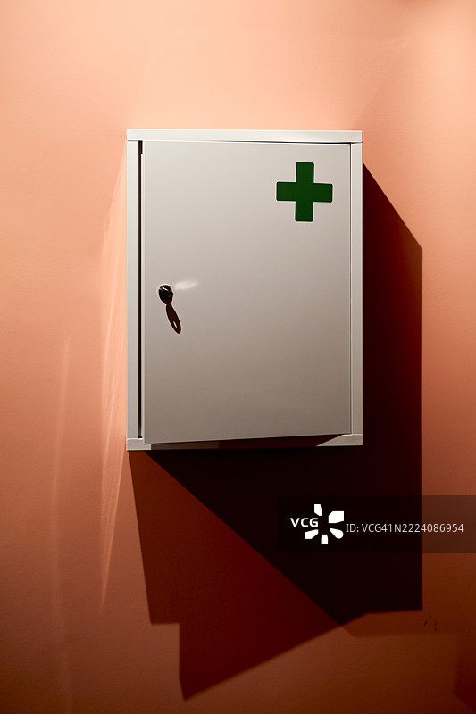 白色急救箱上有绿色十字，投射在桃色墙壁上，影子清晰可见。比利时根特图片素材