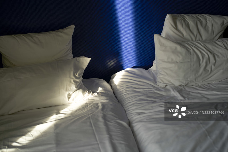 两只白色枕头和床单在阳光下，背景是深蓝色的墙壁。图片素材