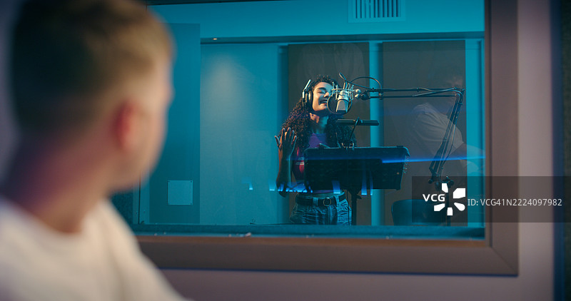 音乐制作人、录音室和拿着麦克风的歌手在片场进行声音制作。女性在音频室中唱歌和听音，进行歌曲、声乐测试或频率测试。图片素材
