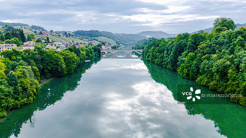 莱茵河的鸟瞰图，展示了历史悠久的拱形铁路桥和森林覆盖的河岸，靠近埃格利绍，宁静的瑞士乡村景象，伴有住宅建筑，夏季旅行与交通概念图片素材