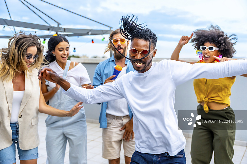 年轻人在热闹的屋顶派对上欢快地跳舞和唱歌，与朋友们一起享受音乐，庆祝夏天的到来。图片素材