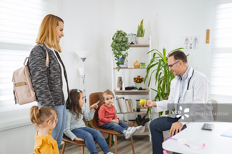 儿科医生在诊所里向孩子们展示一个苹果进行医疗检查图片素材