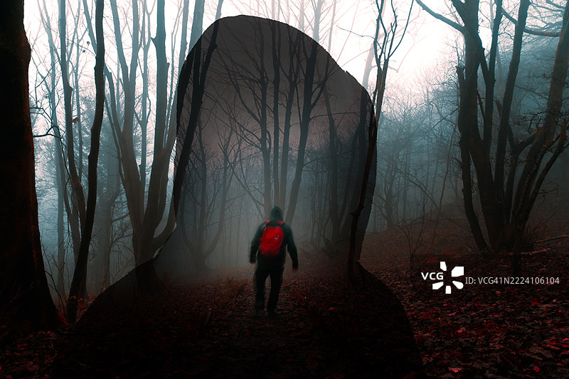A double exposure of a ghost like hooded figure, watching a hiker on a spooky foggy winters day in a forest图片素材