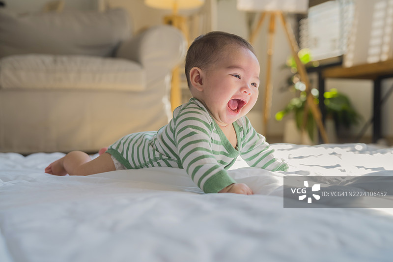 可爱的女孩快乐地在现代阳光明媚的客厅明亮的地板上爬行，周围是温馨而充满光线的氛围。图片素材