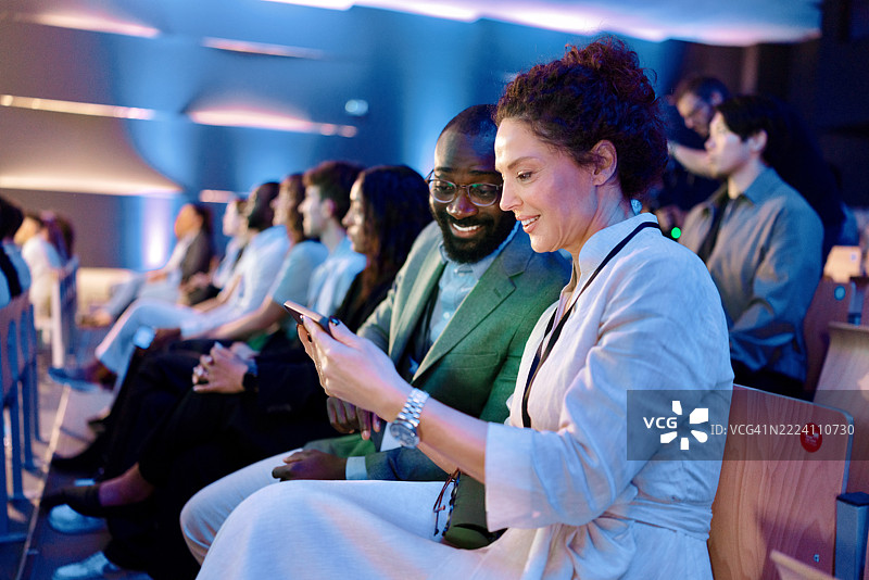 与会者在会议期间坐在一起并查看手机图片素材