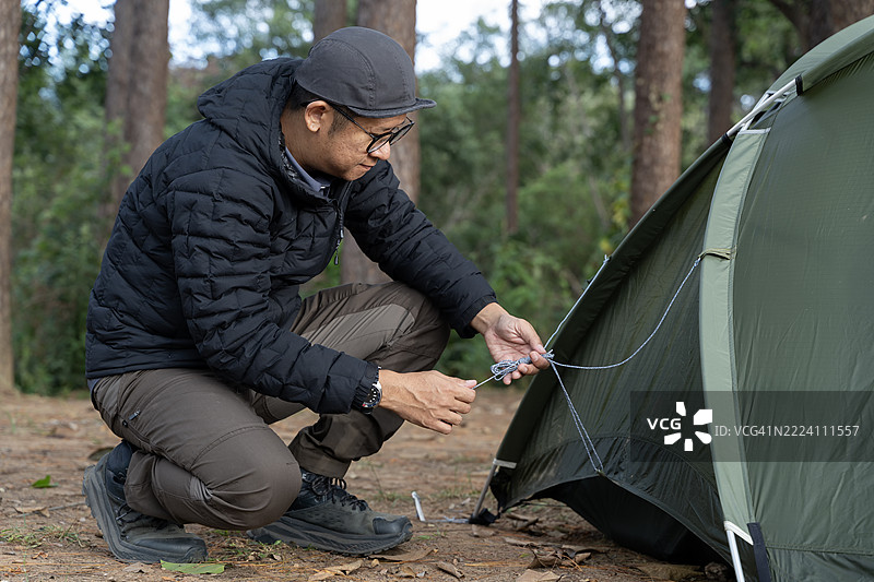 男子在森林中调整帐篷绳索，准备露营场地，户外冒险生活方式，自然荒野旅行图片素材