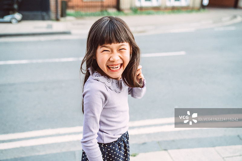 春天的城市街道上，快乐的小女孩在户外欢笑图片素材