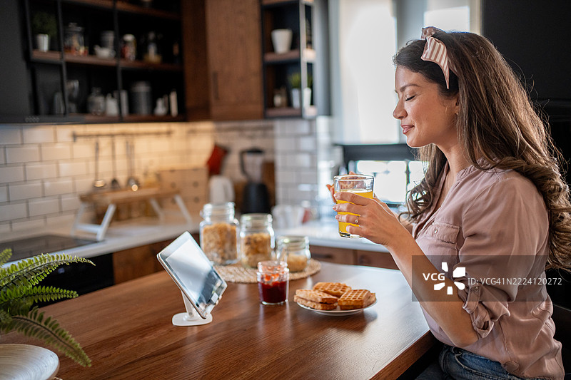 年轻女性享受早餐，同时在平板电脑上查看食谱图片素材