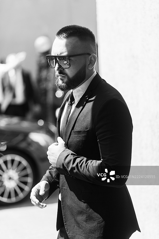 一位年轻的商人正在前往汽车的路上整理他的西装外套。图片素材