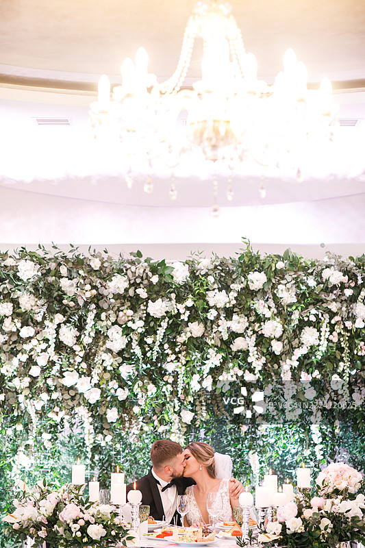 充满爱的新人在美丽的新鲜花朵和蜡烛的环绕中分享一个吻。图片素材