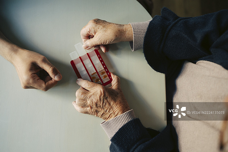 高角度视图，老年女性的手在养老院的桌子上打开药盒图片素材