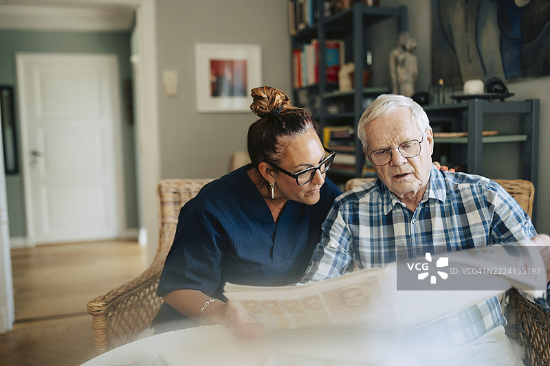 老年男子在养老院里阅读报纸，身旁有女性护理助手。图片素材