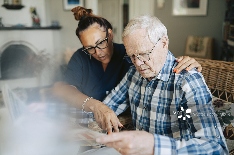 女性医护人员在养老院帮助一位老年男性阅读报纸图片素材