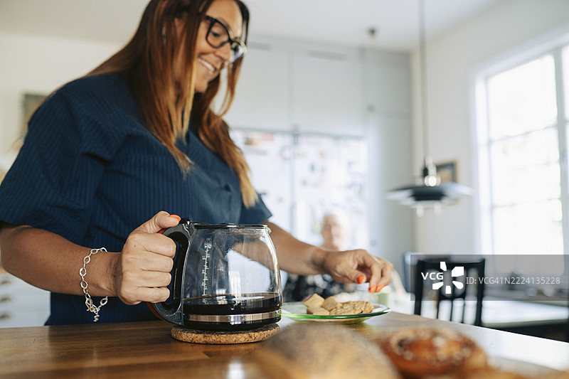 微笑的女性医护人员在养老院的桌子旁拿着咖啡壶。图片素材