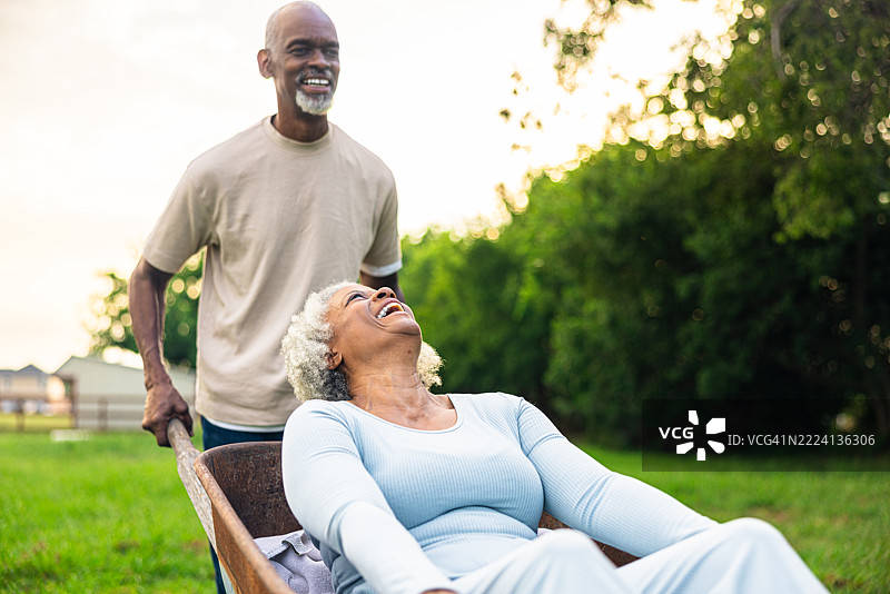 快乐的老年黑人夫妇在后院玩耍，相互推着手推车。图片素材