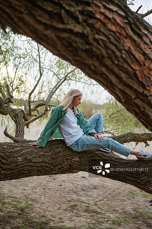 城市短途旅行。女人在海滩上放松，靠在倒下的树枝上。图片素材