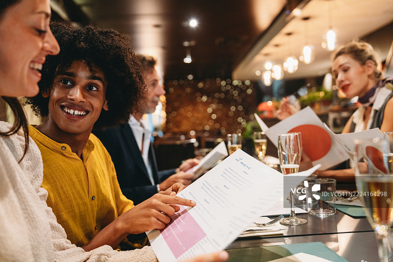 朋友们在高档餐厅享用晚餐并从菜单中选择菜品图片素材