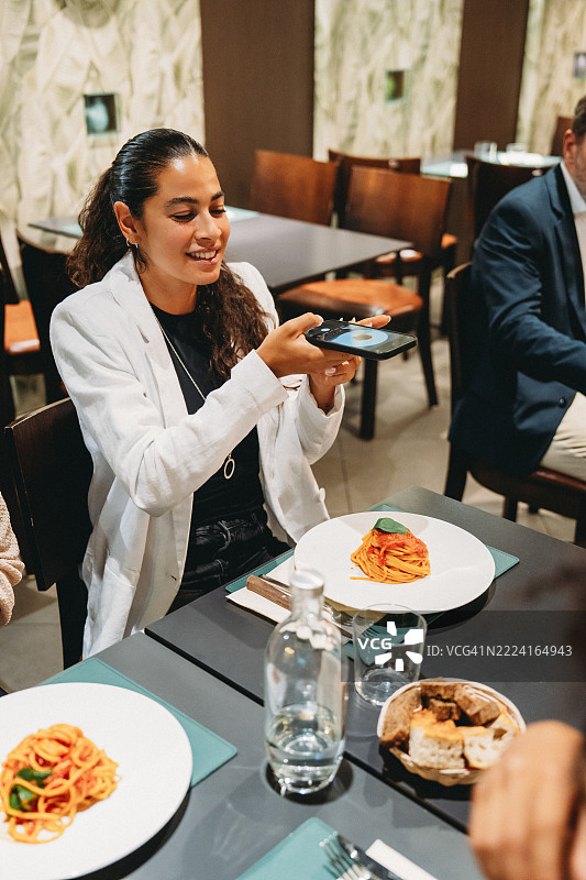 年轻女性在餐厅用智能手机拍摄意大利面照片图片素材