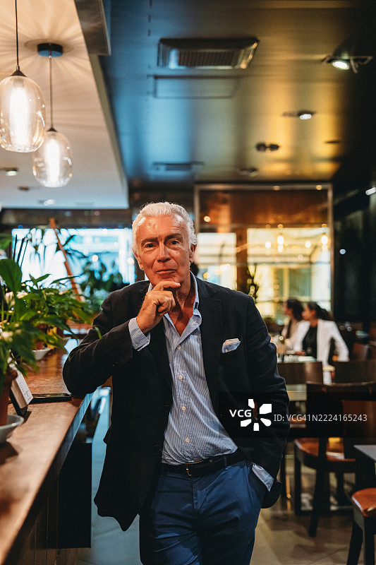 高级商人在餐厅摆姿势，手托下巴思考。图片素材