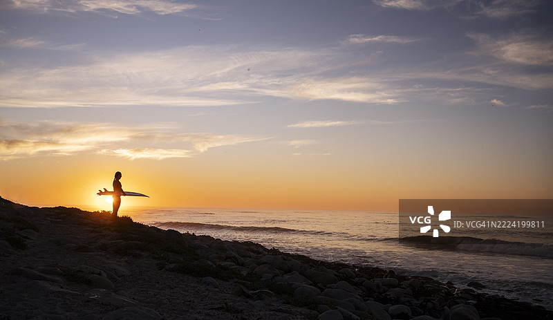 拿着冲浪板的女性剪影在海滩上享受橙色日落的余晖图片素材