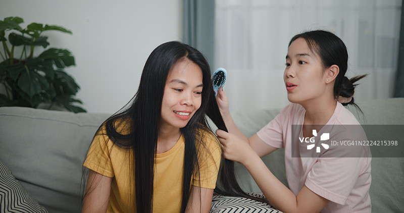 女儿在舒适的客厅沙发上给妈妈梳头，两人一边聊天。图片素材