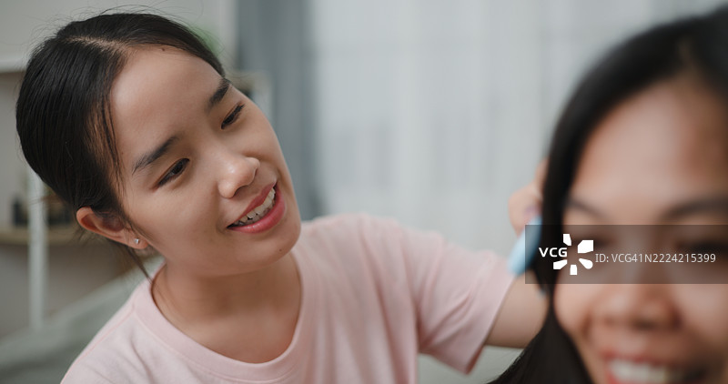 女儿在舒适的客厅沙发上给妈妈梳头，两人一边聊天。图片素材