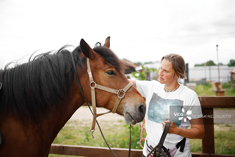 成熟的女性在夏季牧场为马匹准备骑乘图片素材