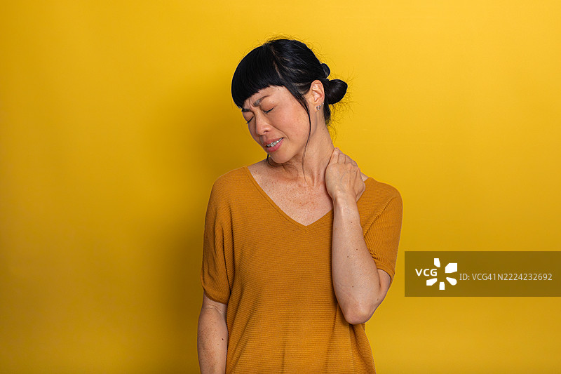 女人在黄色背景下触摸自己的脖子，感到疼痛。图片素材