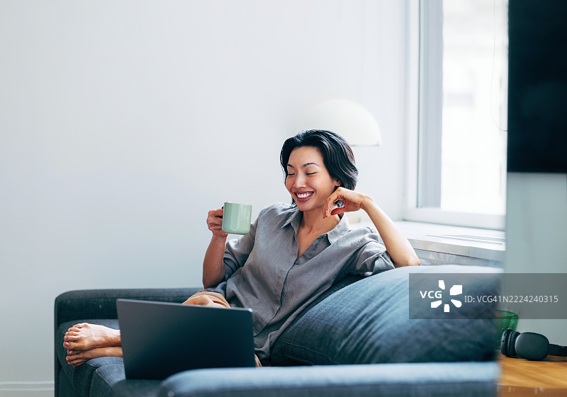 放松的女性在家中一边喝咖啡一边使用笔记本电脑浏览网页图片素材