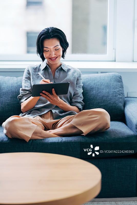 女人坐在沙发上舒适地使用数字平板，神情沉思图片素材