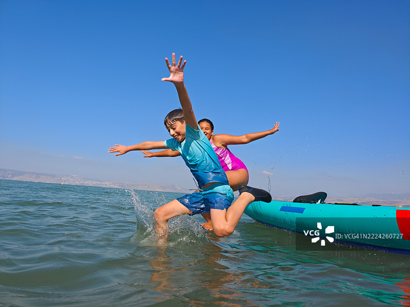 全速跳跃：孩子们在阳光明媚的夏日从皮划艇跳入湖中。图片素材