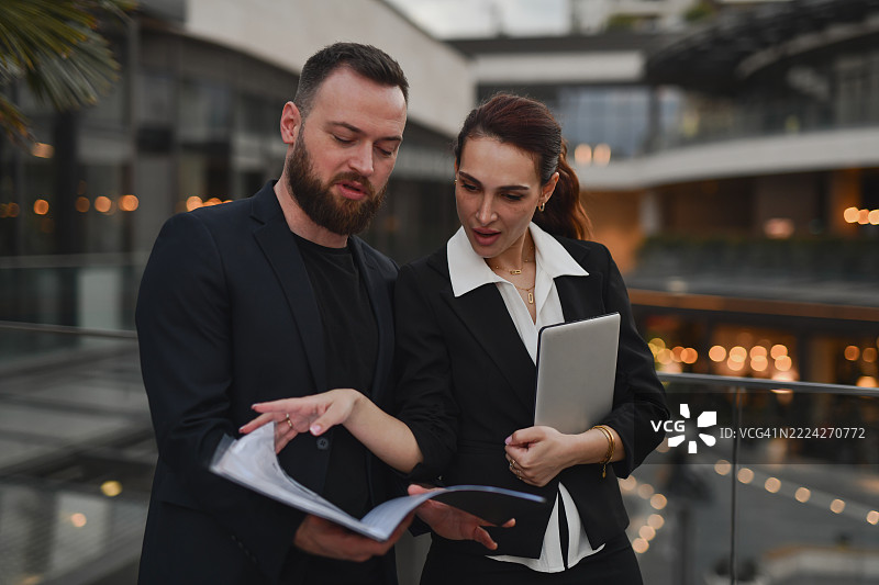 时尚的商务搭档在公司阳台上共同审阅财务报告图片素材