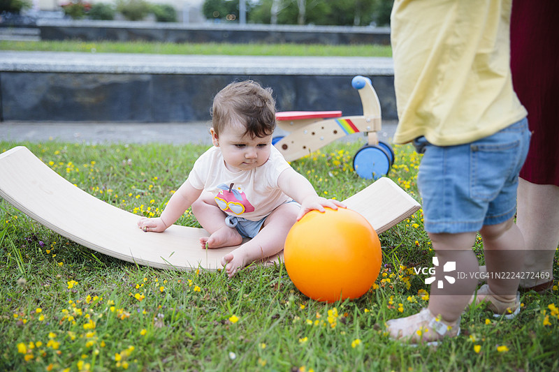 母亲抱着宝宝在公园里走出第一步，旁边另一个宝宝坐着。图片素材