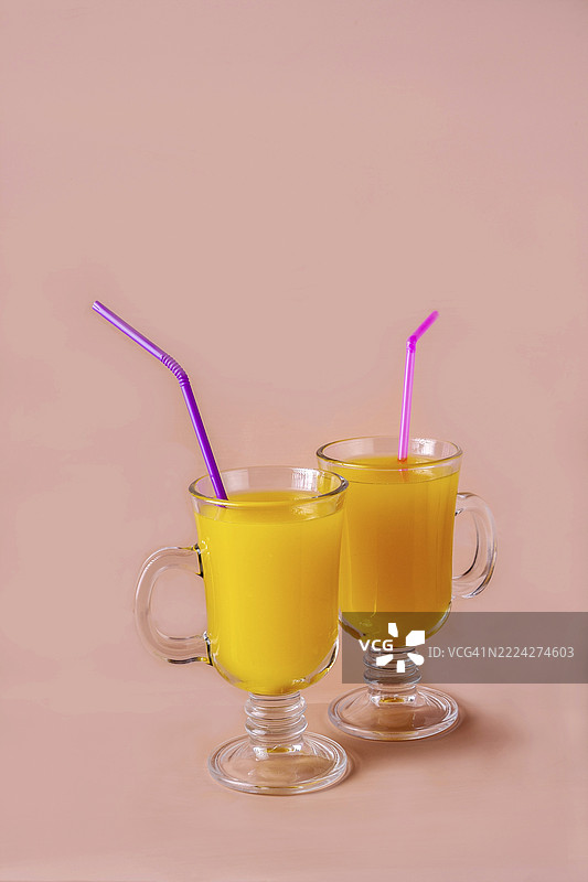 两杯橙汁和鸡尾酒吸管放在米色背景上，留有空白空间图片素材