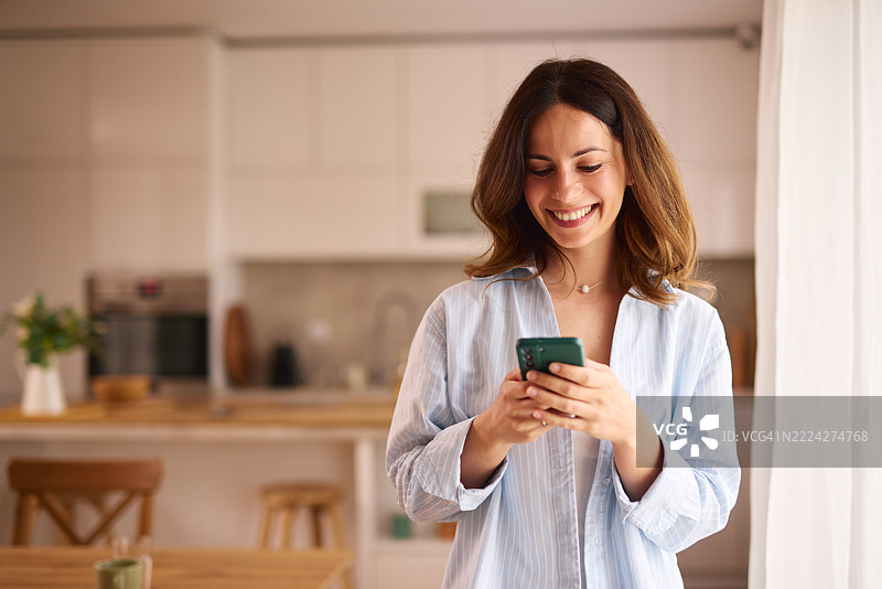 年轻女性在家厨房里微笑着使用智能手机图片素材