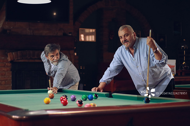 老年朋友们在室内打台球，享受共度时光。图片素材