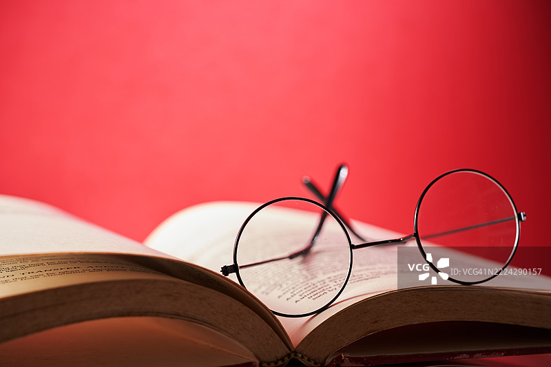 圆形阅读眼镜放在打开的书页上，背景为红色，马来西亚图片素材