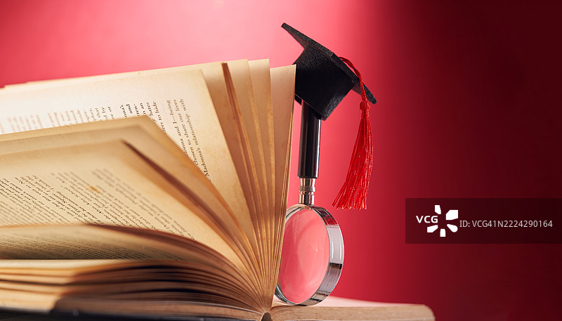 书本上放着一个小学位帽和放大镜，马来西亚图片素材