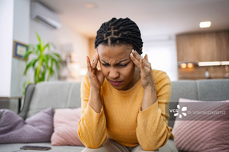 年轻女性因头痛而坐在沙发上，手指轻触太阳穴。图片素材