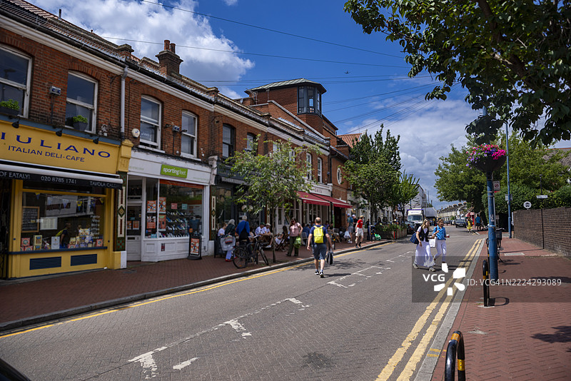 人们在伦敦普特尼的一家咖啡馆外的人行道上走动和坐着，享受轻松的街道氛围。图片素材