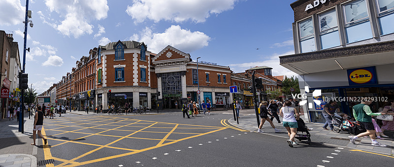 伦敦普特尼大街的繁忙十字路口在明媚的阳光下熙熙攘攘，行人和商店络绎不绝。图片素材