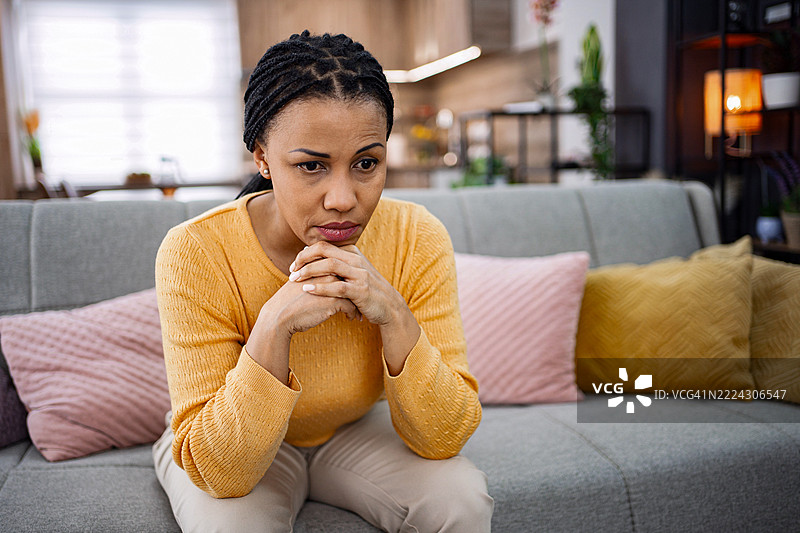 感到孤独和沮丧的悲伤女人坐在家里的沙发上图片素材