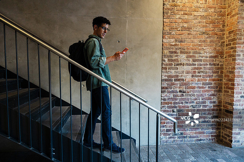 年轻大学生一边走楼梯一边使用智能手机图片素材